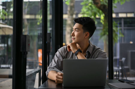 Inspired and handsome millennial Asian businessman thinking and daydreaming while looking out the window in the cafe.の写真素材
