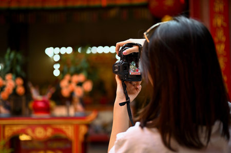 A young Asian female tourist uses her camera to take a photo of a Chinese temple during her sightseeing. back view imageの写真素材