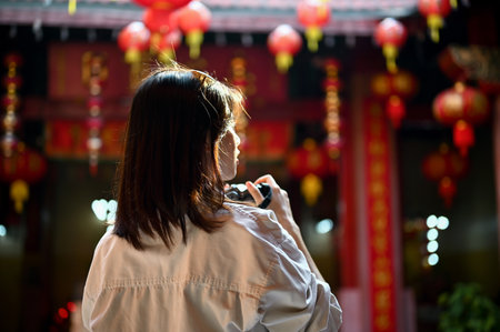 A young Asian female tourist looks at the beautiful historical architecture and uses her camera to take a photo of a Chinese temple during her sightseeing. Back view imageの写真素材