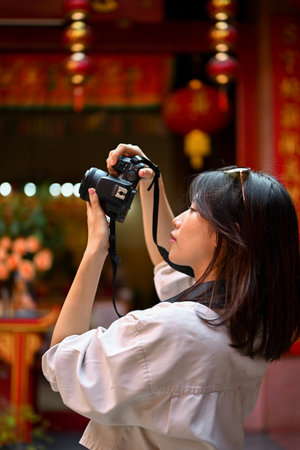 Portrait of a pretty young Asian female tourist taking photos of a beautiful Chinese temple with her camera.の写真素材