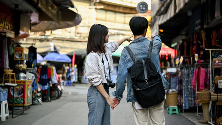 Lovely young Asian tourist couple holding hands and looking for some souvenirs while sightseeing the...