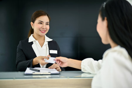 Friendly and beautiful millennial Asian female receptionist greeting and welcoming a customer with...