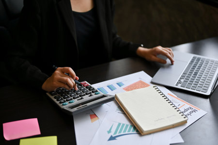 A businesswoman or female business entrepreneur calculates sales using a calculator and laptop computer at her desk in the office. cropped imageの写真素材