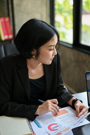 Portrait of a beautiful and successful millennial Asian businesswoman focuses on her work, managing her marketing project in her office.の写真素材