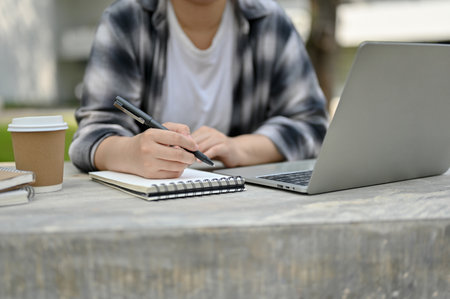 Close-up image of an Asian female college student doing her homework or school project at a campus parkの写真素材