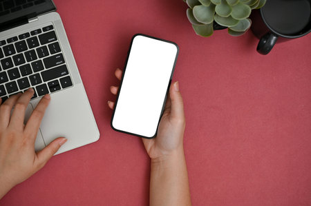 Top view of a businesswoman using her smartphone and laptop computer at her creative red table. smartphone white screen mockupの写真素材
