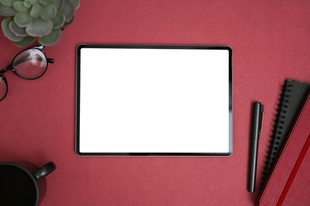 Modern creative workspace top view with digital tablet blank screen mockup, eyeglasses, coffee cup, and stationery on red background.の写真素材