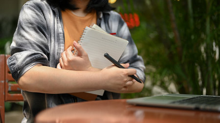 Cropped image of a young Asian female college student in casual clothes sitting outdoor cafe with...