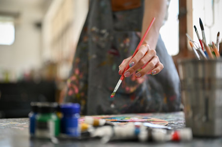 Close-up image of a gay artist wearing an apron dipping his paintbrush in watercolor and making his art work in the studio.の写真素材