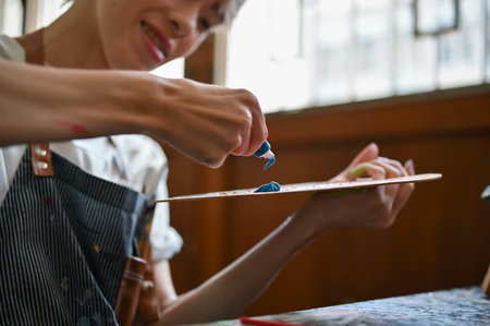 Close-up image of a talented and happy young Asian gay artist squeezing a watercolor on an art palette while preparing colors for his artwork in the studio.の写真素材