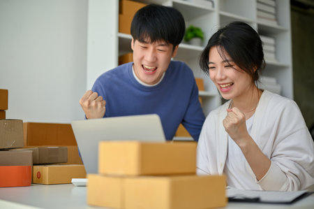 Cheerful and successful young Asian couple, online business owners are showing their fists and celebrating their online business success together. SME, E-commerce, Online sellingの写真素材