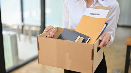 Cropped image of a female office worker holding a cardboard box with her stuff and her resignation letter. unemployment, being firedの写真素材