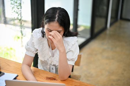 Stressed and tired young Asian female office worker suffering from headache after a long day at work. overworked, depressed, upset, frustratedの写真素材