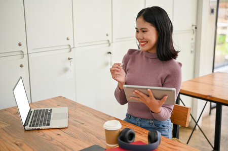 Attractive and confident young Asian female college student remote working in the coffee shop,...