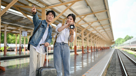 A lovely young Asian couple is waiting for their train at the railway station, traveling on holidays together. Tourist, Travelers, Commutersの写真素材