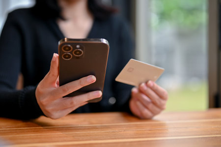 Close-up image of a female holding a credit card and smartphone, using her mobile banking while...