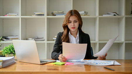 A beautiful young Asian businesswoman or female financial manager focuses on examining financial...