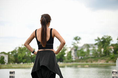 Back view, A sporty and healthy-fit Asian woman in sportswear takes a deep breath, looks at the view in front of her, and rests after a long run outdoors.の写真素材