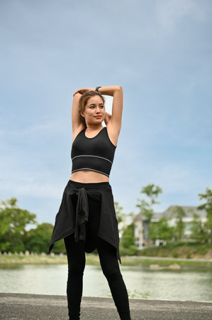 A portrait of a beautiful young Asian woman in sportswear is stretching her arms, warming up her body before running outdoors.の写真素材