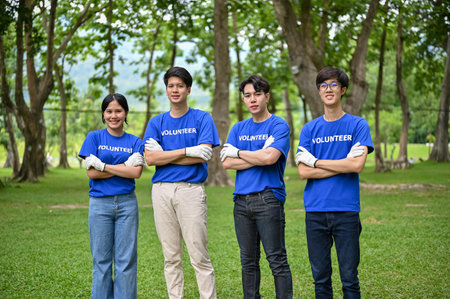 A group of happy young Asian volunteers in uniform standing in the public park with their arms...