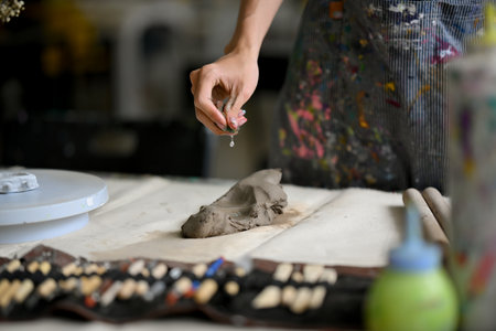 Close-up image of a male artist potter kneading raw clay to make an earthenware at his worktable in his pottery studio. handicraft, pottery workshop, sculptureの写真素材