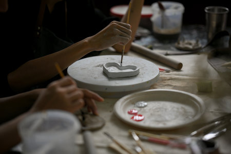 Close-up image of a man enjoys painting a ceramic plate in a creative handicraft workshop with his friend. Handicraft workshop conceptの写真素材