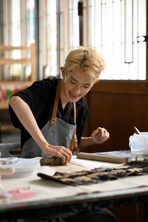 A happy and attractive young Asian gay man enjoys making earthenware or sculpting an ornament with...