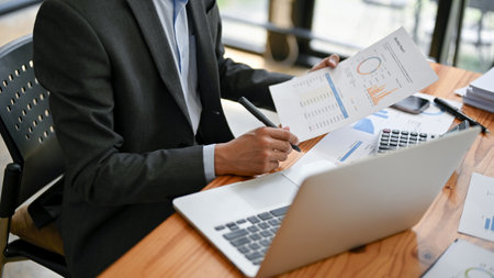 Close-up image of a smart and professional businessman or male analyst in a formal business suit is examining and analyzing business financial reports at his desk.の写真素材