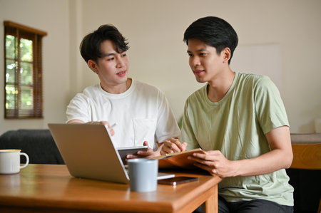 A smart young Asian male college student is explaining, tutoring, and helping his friend with math at home. Education conceptの写真素材