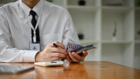 Close-up image of a professional Asian male banker counting US dollar bills at his desk in the...