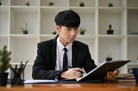 A professional and handsome Asian male lawyer in a formal suit is writing a notice letter at his desk in the office. lawsuit, notice letter, prosecution, judgementの写真素材