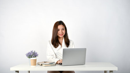An attractive millennial Asian businesswoman working on her tasks on her laptop at her desk against an isolated white background.の写真素材