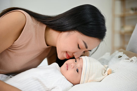 Beautiful asian mom lay down with her baby, comforting her son on bed. Mother and child conceptの写真素材