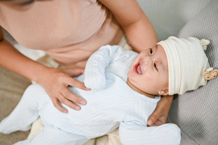 Close up view of baby being hold by mother while relaxing on the sofa, spending time with her son.