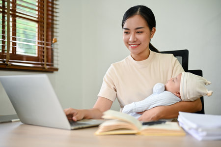 Young beautiful Asian mother working at home and holding her baby in her arms.の写真素材