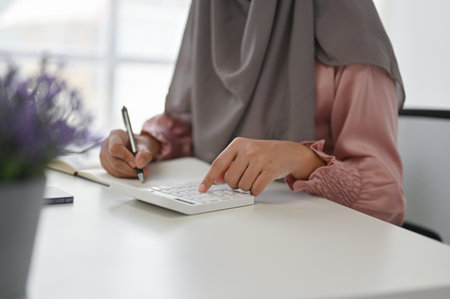 Close up view of young Muslim businesswoman using calculator while working in her office room.の写真素材