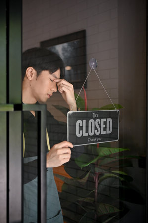 Depressed young coffee shop owner closing his coffee shop, closing down the business.の写真素材