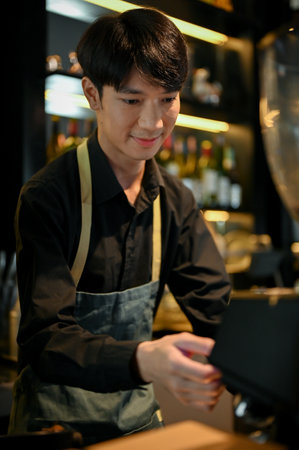 Young handsome Asian male barista making a cup of coffee for his customer in dark modern coffee shopの写真素材