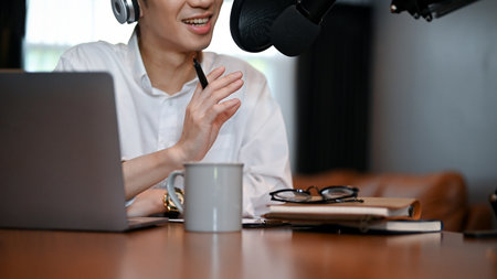 Young podcast artist wearing headphones talking into microphone at studio. Making podcast for...