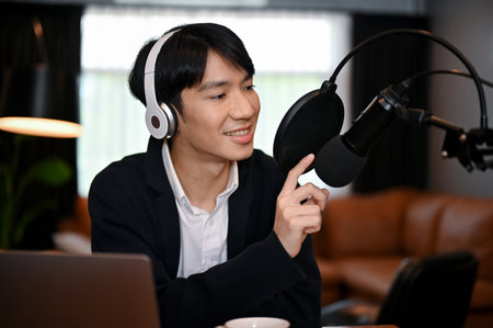 Young podcast artist wearing headphones talking into microphone at studio. Making podcast for audianceの写真素材