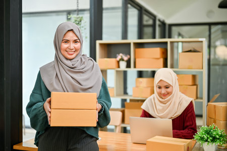 A happy young Asian Muslim female online seller working with her employee in the office. SME business, online shop ownerの写真素材