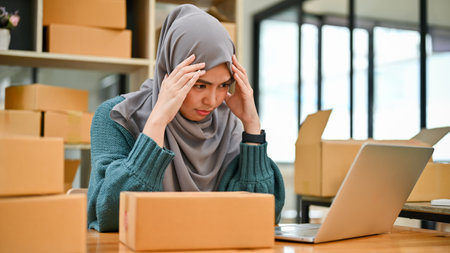 Stressed Muslim online business owner feeling upset and unhappy about the sale and orders in her workplaceの写真素材