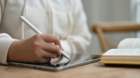 Close-up image of a woman holding a stylus pen, writing or taking notes on her digital tablet, remote woking at a coffee shop.の写真素材