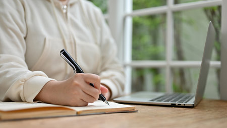 Close-up image of a female in casual clothes writing something on a book, taking notes or writing on her diary while remote working at a coffee shop.の写真素材
