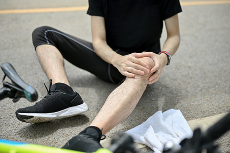 Close-up image of an injured male cyclist in sportswear fell off the bike while biking along country roads. knee pain, knee bleeding, injured kneeの写真素材