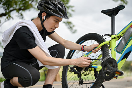 A professional young Asian male cyclist fixes his bike chain on the street after riding on country roads. maintenance, repairの写真素材