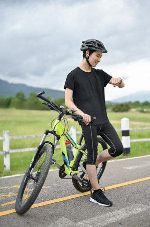 A handsome and happy young Asian man in sportswear and a bike helmet stands with his bike on the...