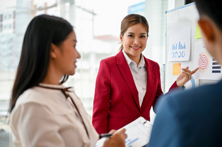 A confident millennial Asian businesswoman presented her marketing project on a whiteboard to her team in the meeting. creative brainstorming meeting conceptの写真素材
