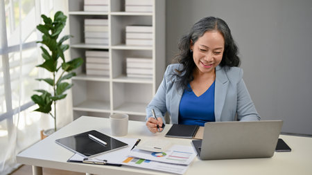 A successful and happy Asian senior businesswoman or female CEO working on her business works at her desk in her private office.の写真素材
