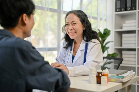 A caring and smiling Asian senior female doctor holding a patient's hands to comfort and reassure during the medical checkup at a hospital.の写真素材